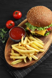 Photo of Delicious burger with beef patty, tomato sauce and french fries on black wooden table, above view