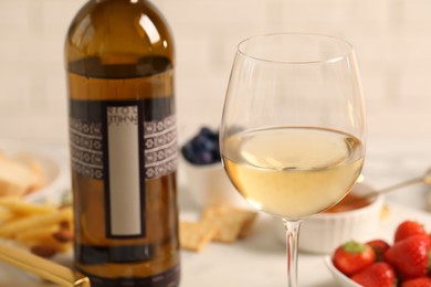 Photo of Glass of wine near bottle and delicious snacks on white table, closeup