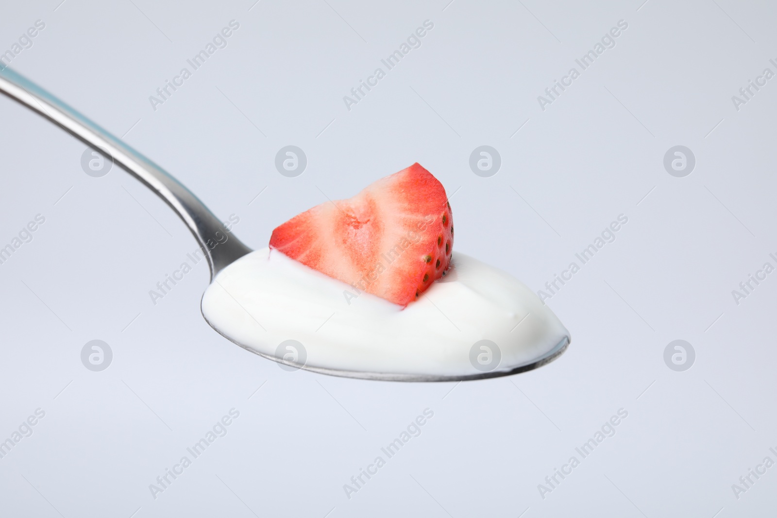 Photo of Delicious natural yogurt with fresh strawberry in spoon on light background