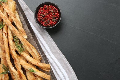 Photo of Tasty grissini with rosemary and mixed peppercorns on black table, flat lay. Space for text