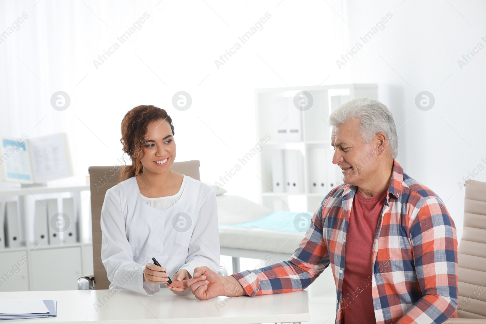 Photo of Doctor taking patient's blood sample with lancet pen in hospital. Diabetes control