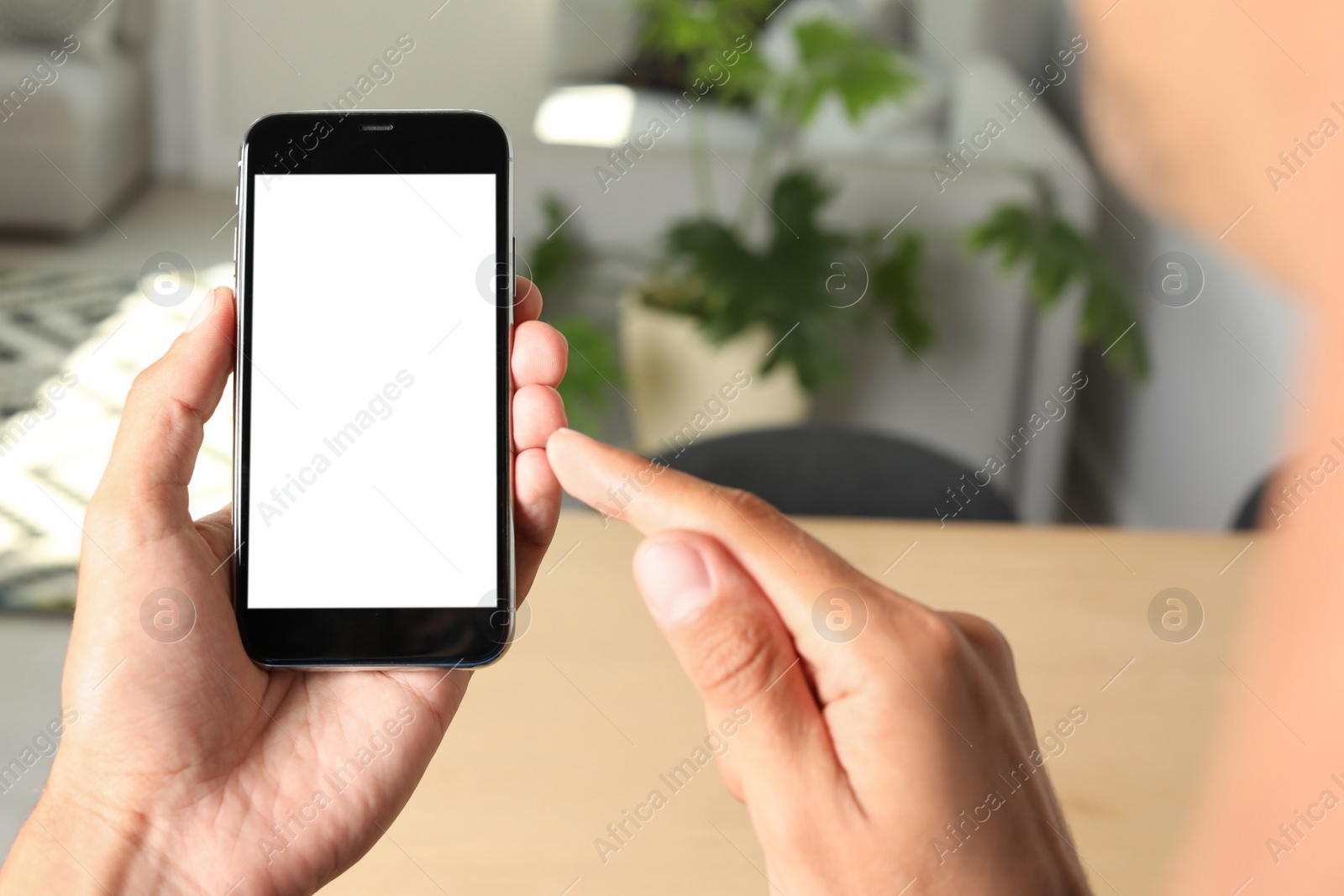 Photo of Young man holding mobile phone with blank screen on blurred background, closeup