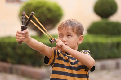 Photo of Little boy playing with slingshot in park