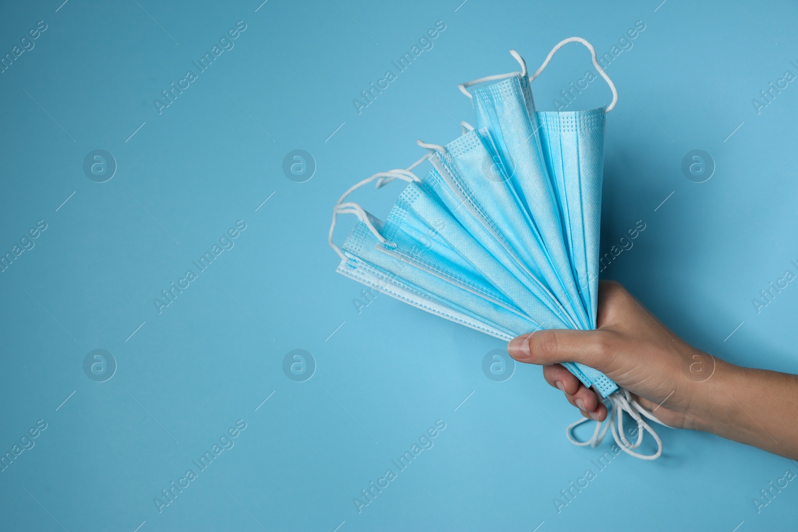 Photo of Woman holding disposable face masks on light blue background, closeup with space for text. Protective measures during coronavirus quarantine