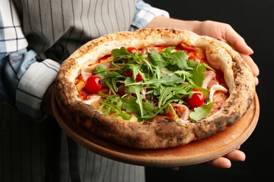 Photo of Woman holding tasty pizza with meat and arugula on black background, closeup