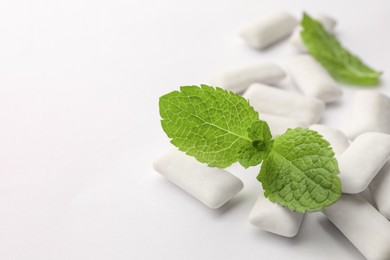 Tasty chewing gums and mint leaves on white background, closeup. Space for text