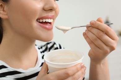 Photo of Happy woman eating tasty yogurt indoors, closeup