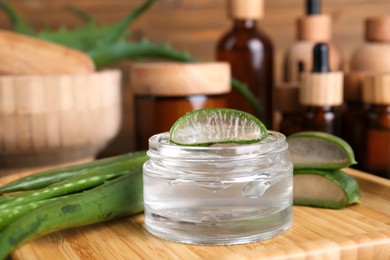 Photo of Jar with natural gel and fresh aloe vera leaves on wooden tray, closeup
