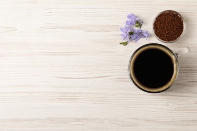 Photo of Glass cup of delicious chicory drink, granules and flowers on white wooden table, flat lay. Space for text