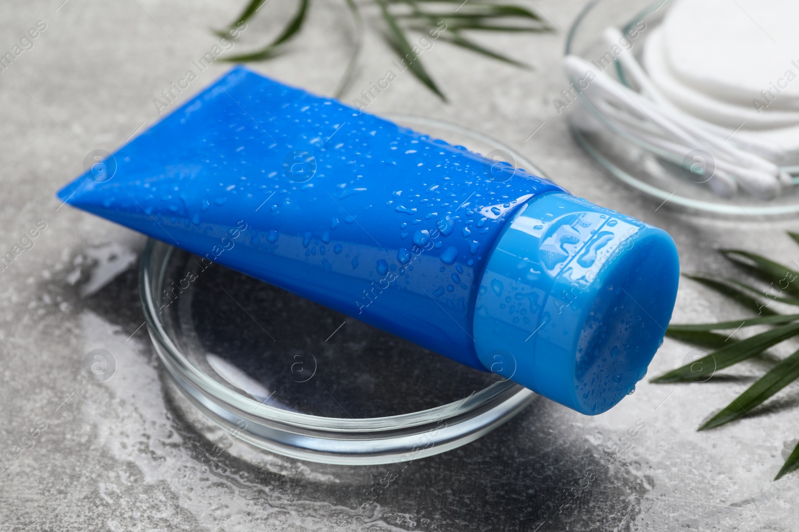 Photo of Tube of face cleansing product and green leaves on light grey table, closeup