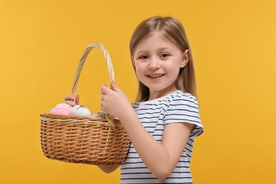 Photo of Easter celebration. Cute girl with basket of painted eggs on orange background