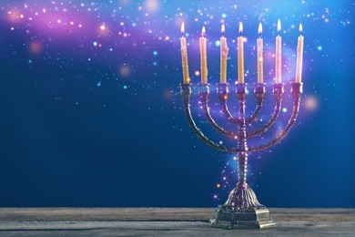 Image of Hanukkah celebration. Menorah with burning candles on wooden table against blue background, space for text