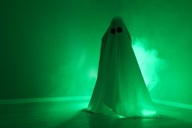 Creepy ghost. Woman covered with sheet in green light, space for text