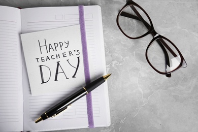 Photo of Paper with inscription HAPPY TEACHER'S DAY, notebook and eyeglasses on grey table, flat lay