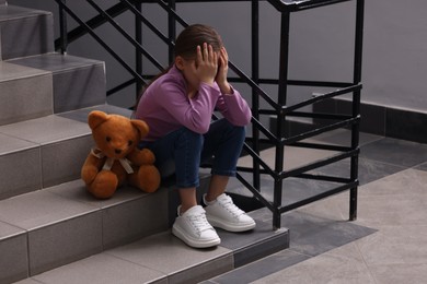 Photo of Child abuse. Upset girl with toy sitting on stairs