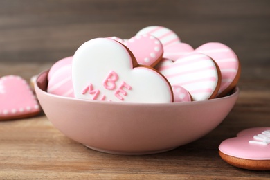 Photo of Decorated heart shaped cookies in bowl on wooden table, closeup. Valentine's day treat