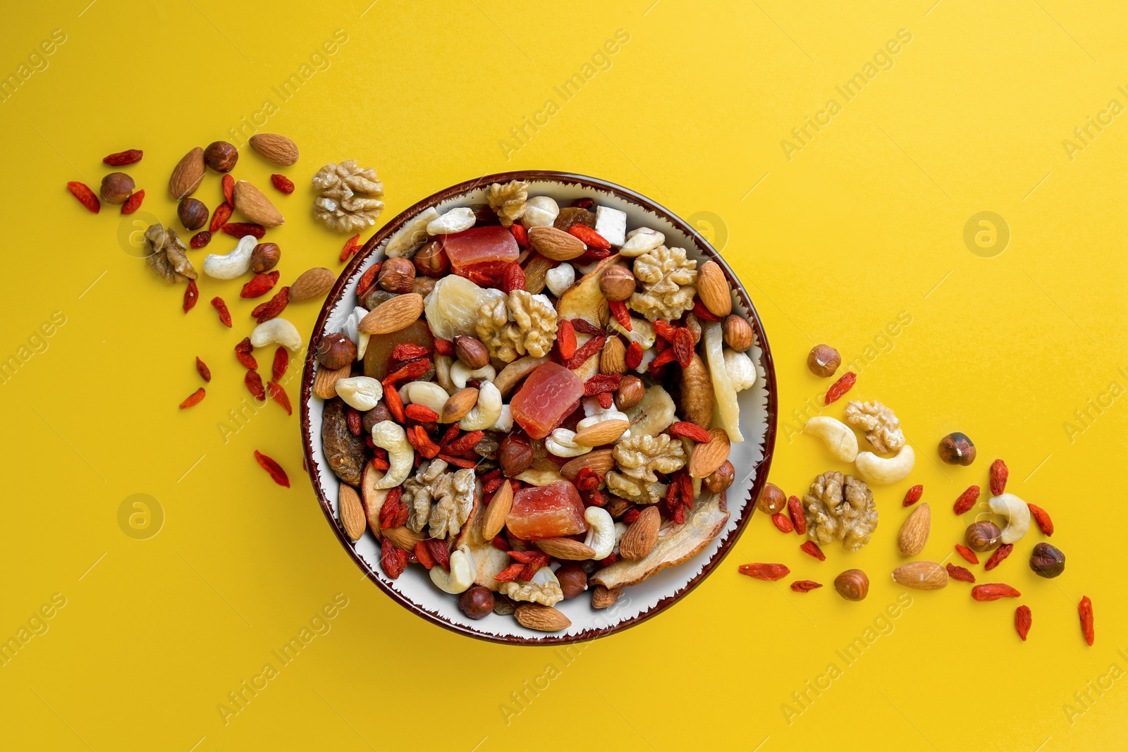 Photo of Bowl with mixed dried fruits and nuts on yellow background, flat lay