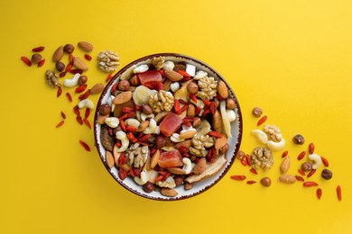 Bowl with mixed dried fruits and nuts on yellow background, flat lay