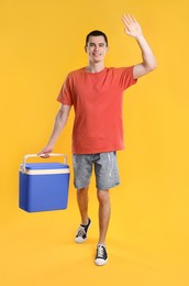 Man with blue cool box walking and greeting someone on orange background