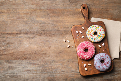 Photo of Top view of yummy donuts with sprinkles on wooden table, space for text