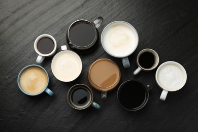 Photo of Different coffee drinks in cups on dark textured table, flat lay