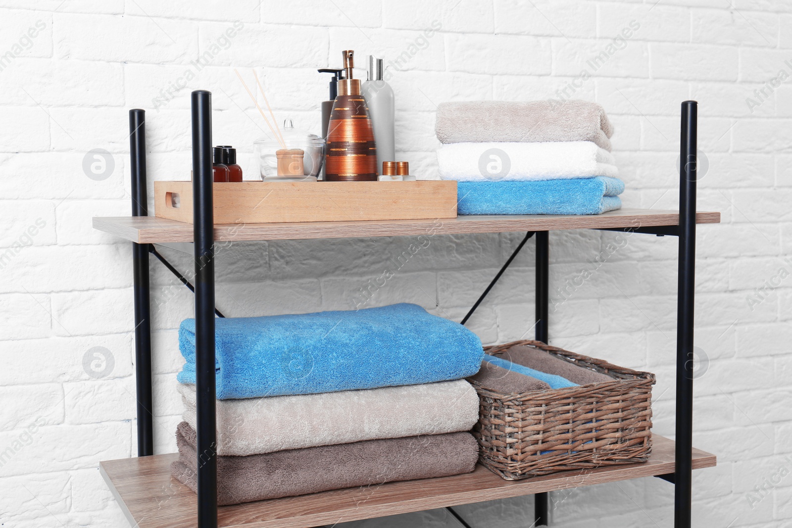 Photo of Shelving unit with clean towels and toiletries near brick wall