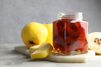 Photo of Tasty homemade quince jam in jar and fruits on grey textured table, closeup. Space for text