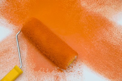 Photo of Roller brush and strokes of orange paint on white background, top view