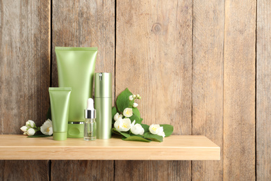 Photo of Set of cosmetic products and flowers on shelf near wooden wall, space for text