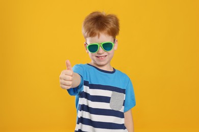 Photo of Cute little boy with sunglasses on yellow background