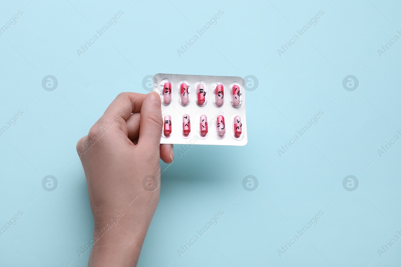 Photo of Woman holding antidepressants with different emoticons on light blue background, top view