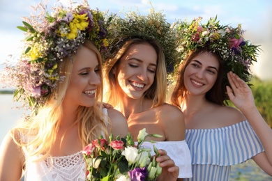 Young women wearing wreaths made of beautiful flowers outdoors on sunny day