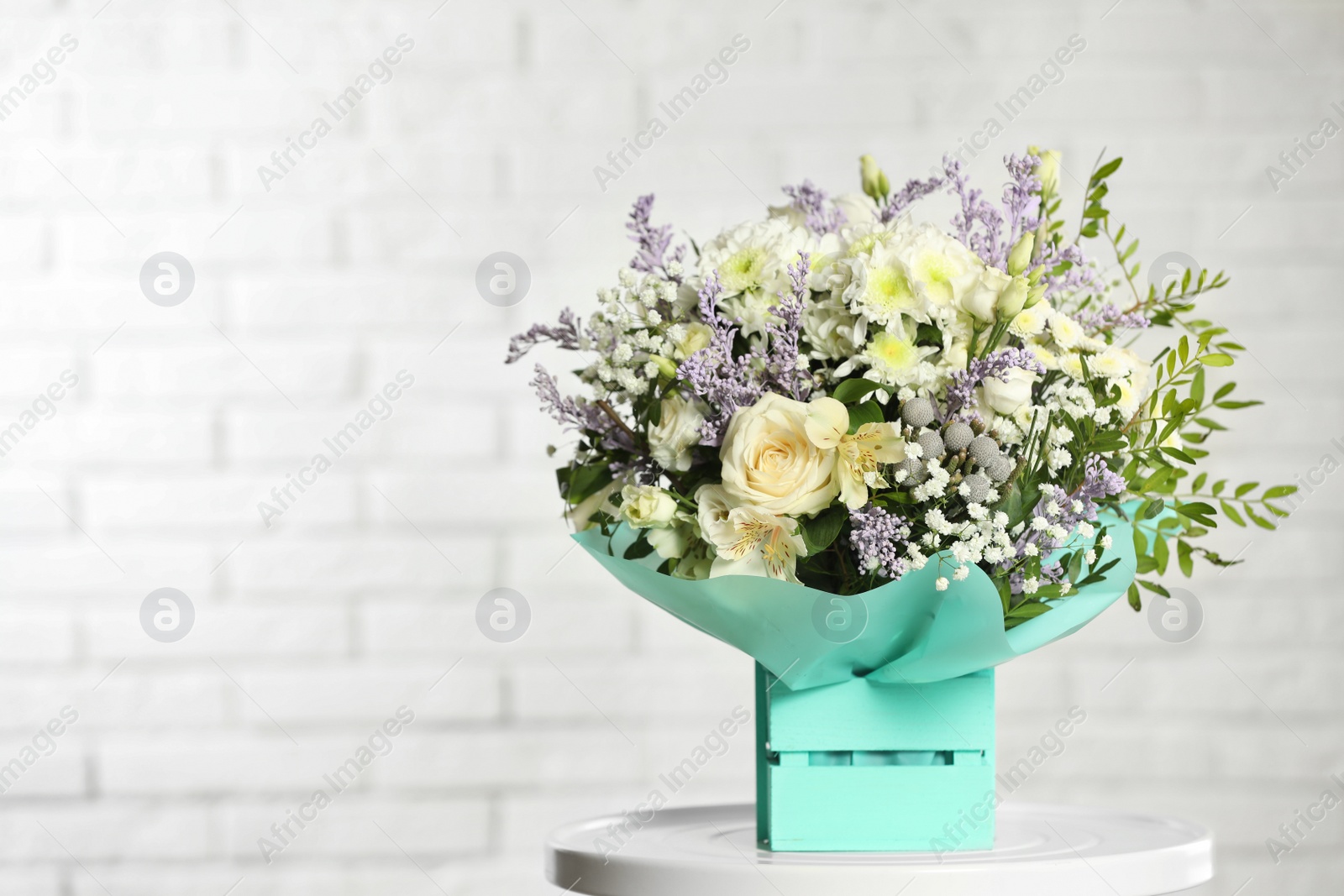 Photo of Beautiful bouquet of flowers in decorative crate on table against light background. Space for text