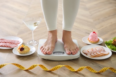 Food, alcohol left after holidays and woman with measuring tape standing on scales indoors, closeup. Overweight problem