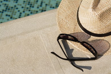 Photo of Stylish hat and sunglasses near outdoor swimming pool on sunny day, above view. Space for text