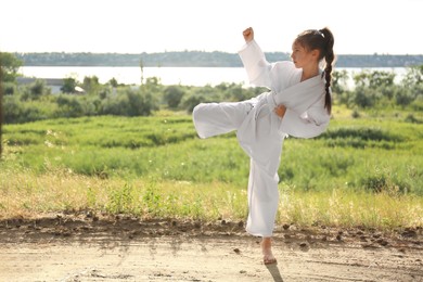 Photo of Cute little girl in kimono practicing karate outdoors