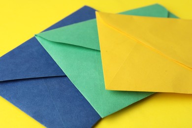 Photo of Colorful paper envelopes on yellow background, closeup