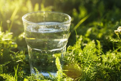 Photo of Glass of fresh water on green grass outdoors, closeup