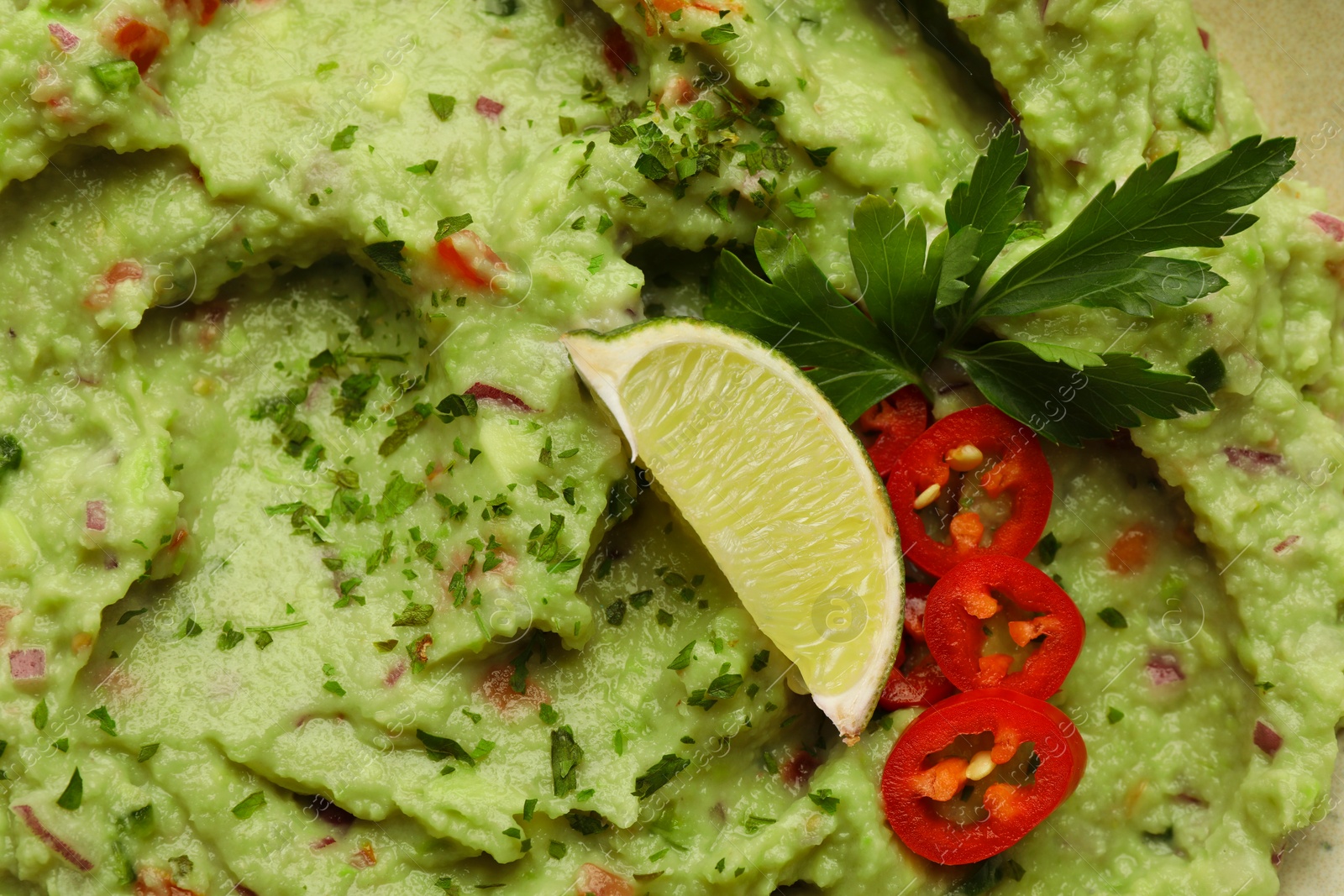 Photo of Delicious guacamole with lime, pepper and parsley as background, top view