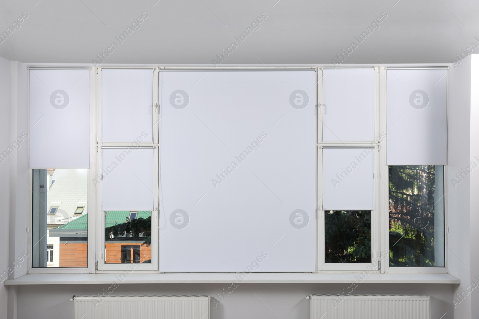 Photo of Large window with white roller blinds indoors
