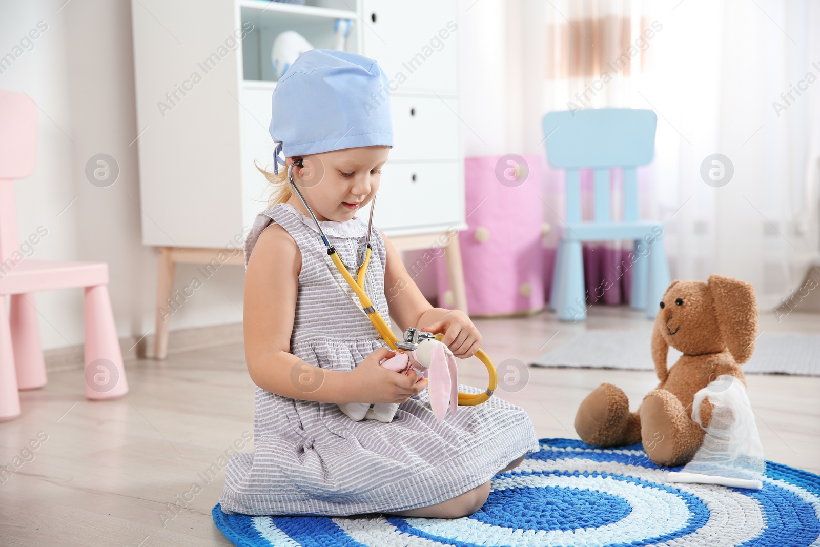 Photo of Cute child imagining herself as doctor while playing with stethoscope and toy bunny at home