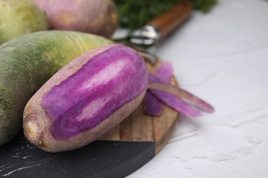 Photo of Purple and green daikon radishes on white textured table, closeup. Space for text