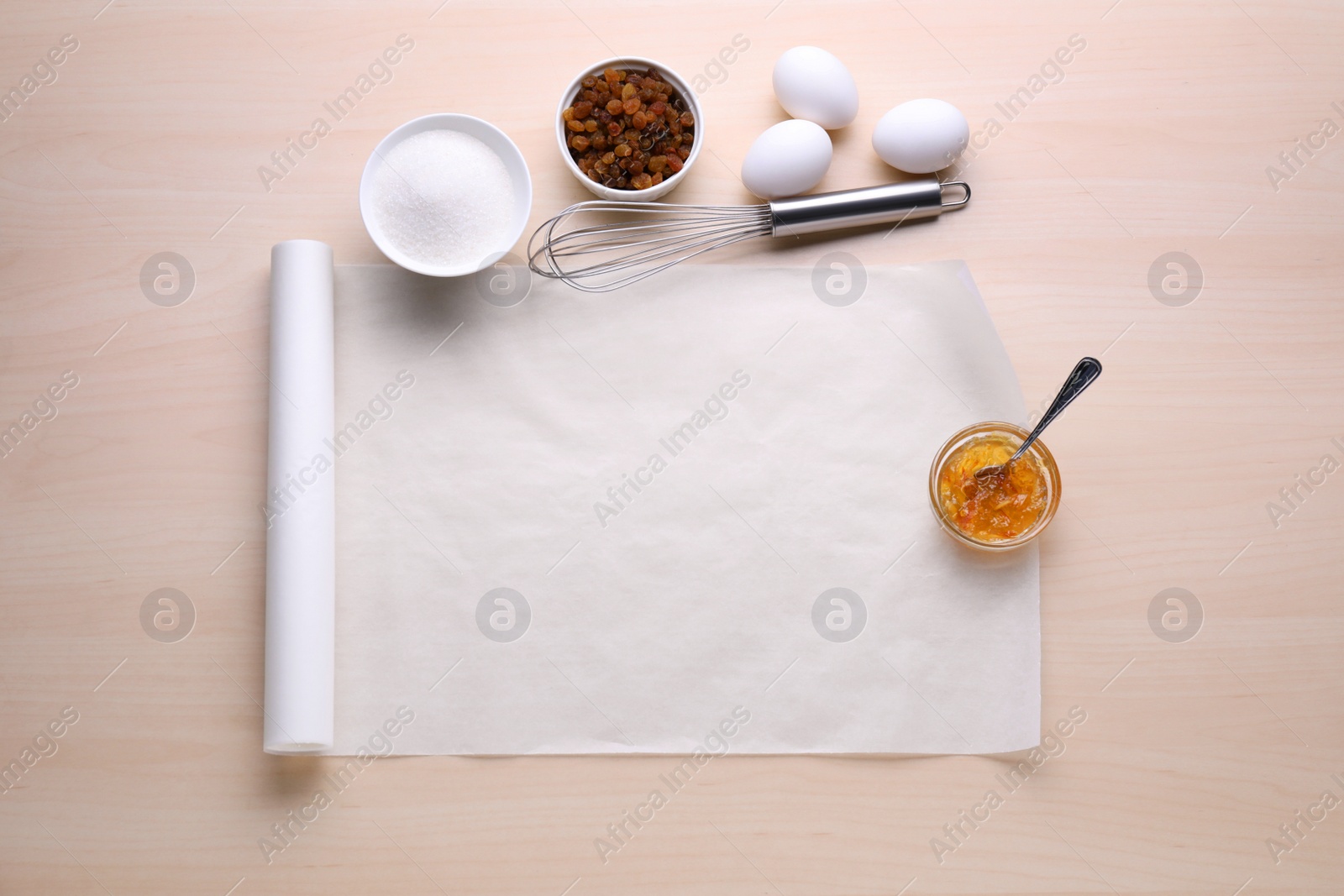 Photo of Baking parchment paper and different ingredients on wooden table, flat lay. Space for text