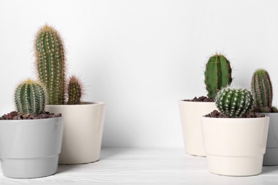 Photo of Different cacti in pots on white wooden table