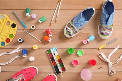 Photo of Sneakers and painting supplies on wooden table, flat lay. Customized shoes