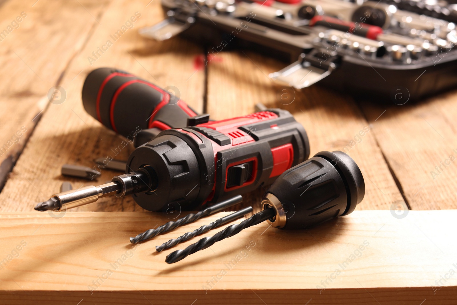 Photo of Electric screwdriver with bits and drills on wooden table, closeup