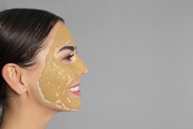 Photo of Young woman with clay mask on her face against grey background, space for text. Skin care