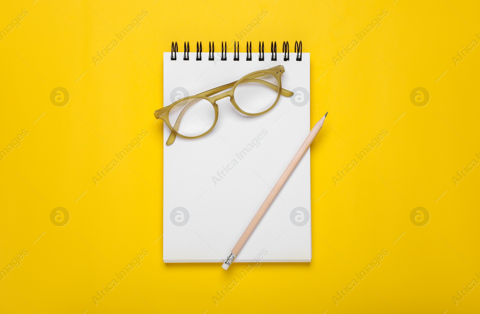 Photo of Office notebook, eyeglasses and pencil on yellow background, top view