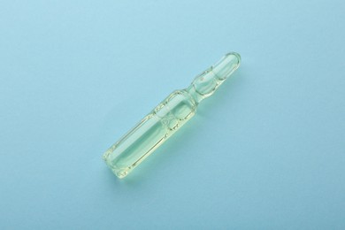 Glass ampoule with liquid on light blue background, top view