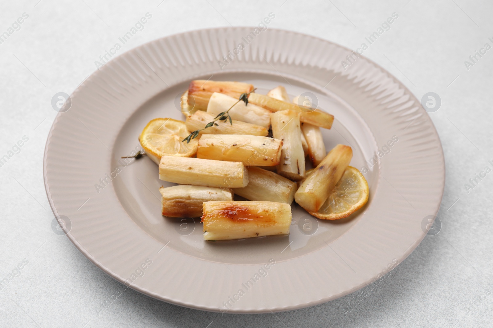 Photo of Plate with baked salsify roots, lemon and thyme on light grey table, closeup